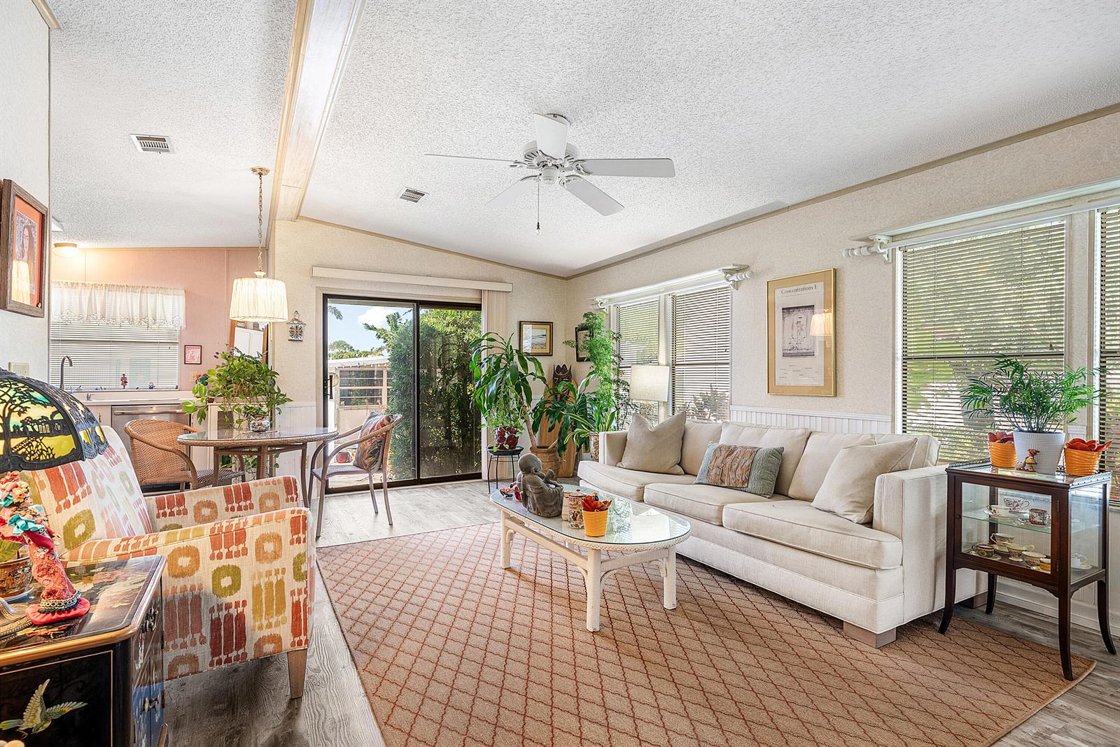 A living room features a beige sofa, patterned armchair, glass coffee table, and sliding glass doors — 4 East Cedar Drive, Briny Breezes FL 33435, BRINY BREEZES, FL