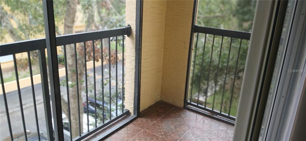 A tiled balcony features black metal railings overlooking a parking area and trees — 5606 PINNACLE HEIGHTS CIRCLE UNIT 306, TAMPA, FL