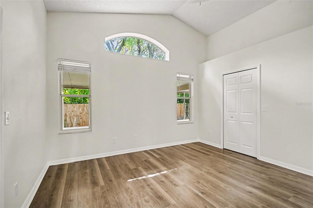 An empty room with wood-look flooring, white walls, two windows, an arched transom, and closet — 10131 RIVERS TRAIL DRIVE, ORLANDO, FL