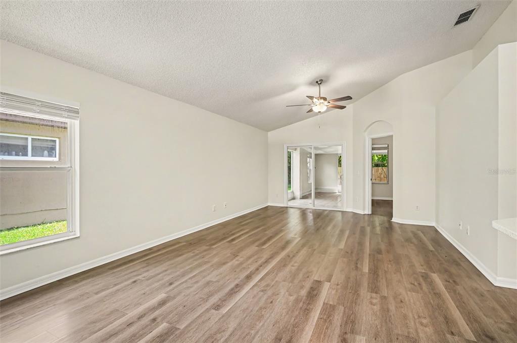 An empty living room features light-colored walls, wood-look flooring, a ceiling fan, and sliding doors — 10131 RIVERS TRAIL DRIVE, ORLANDO, FL