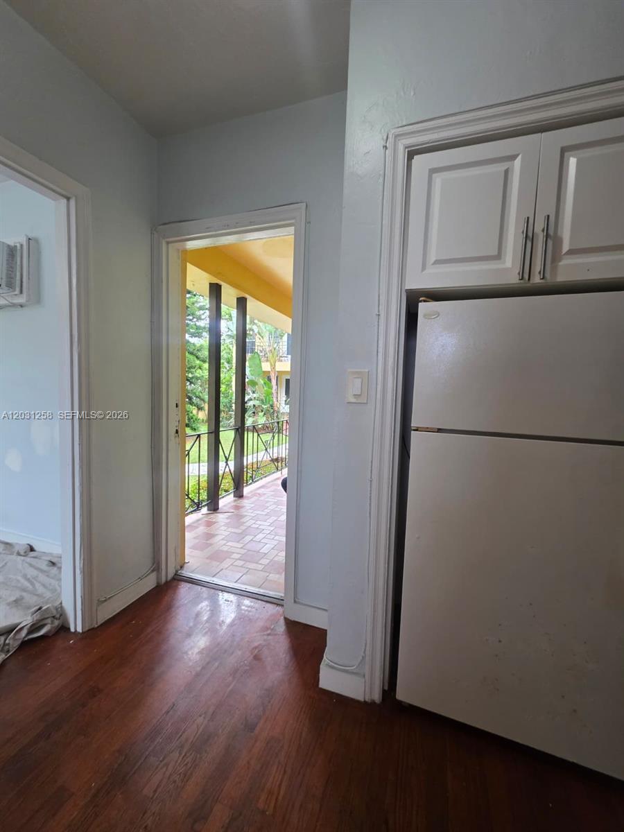 A kitchen area features a white refrigerator, wood flooring, and a doorway leading to a balcony — 8024 Harding Ave # 1A, Miami Beach FL 33141, MIAMI BEACH, FL
