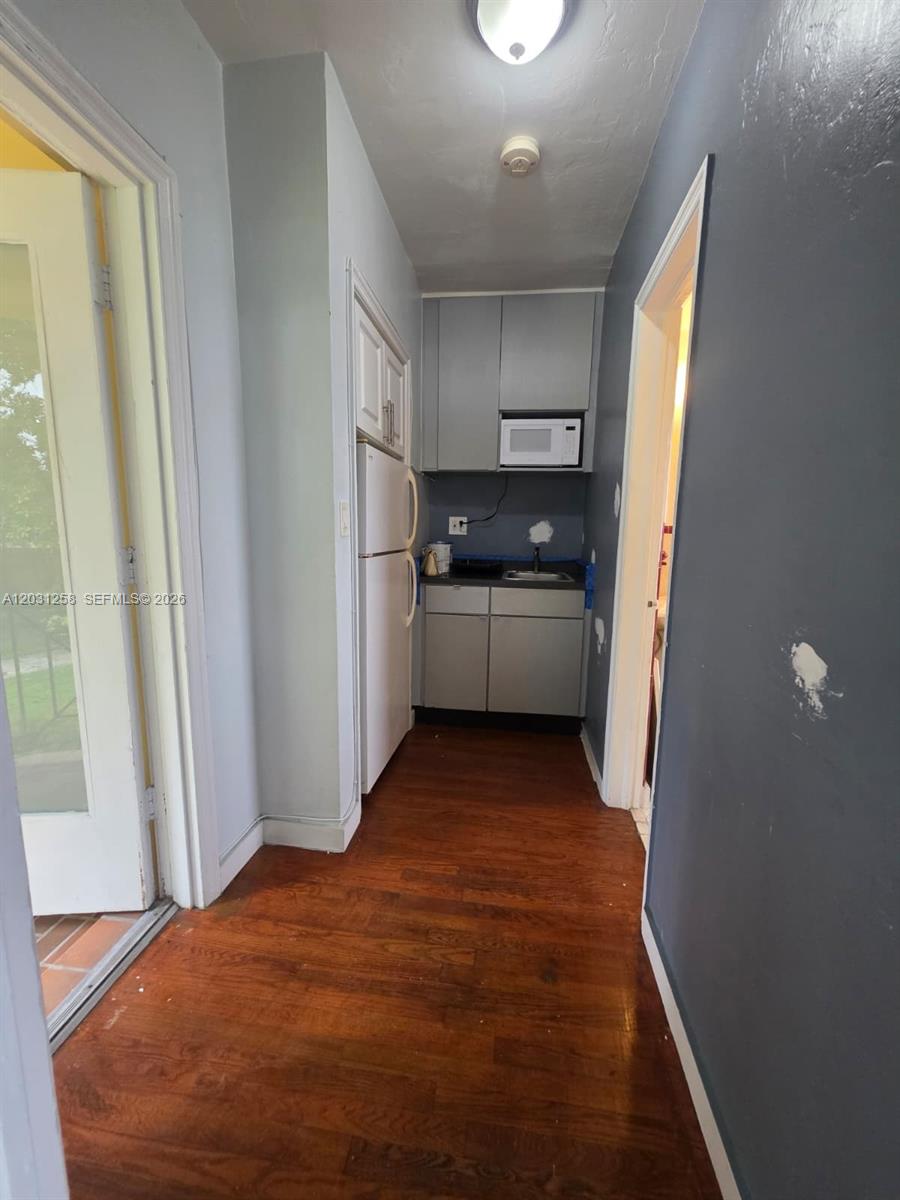 A small kitchen features gray cabinets, a white refrigerator, and dark wood flooring — 8024 Harding Ave # 1A, Miami Beach FL 33141, MIAMI BEACH, FL