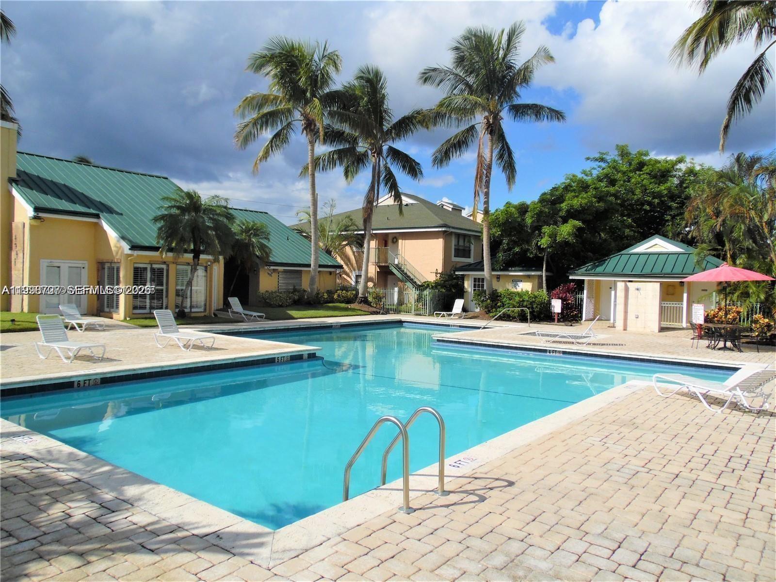 An outdoor swimming pool with lounge chairs and palm trees sits between residential buildings — 8719 NW 39th St # 8719, Sunrise FL 33351, SUNRISE, FL