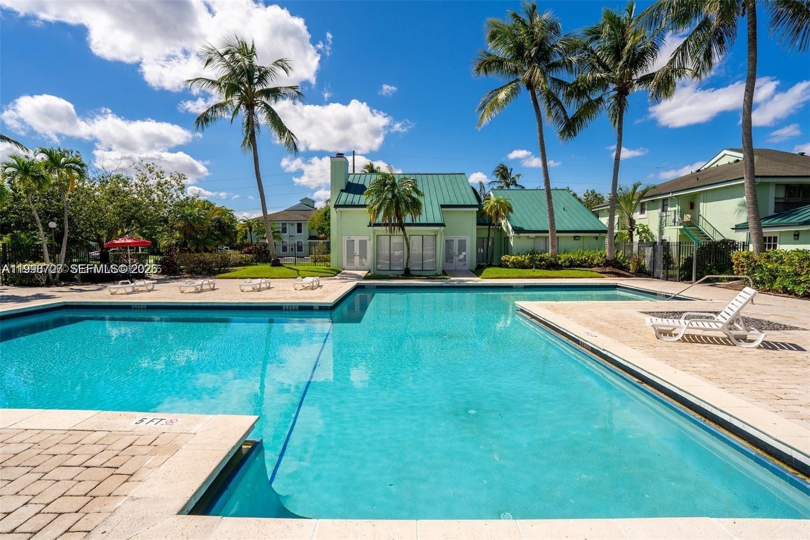A swimming pool sits in front of a green building with a metal roof — 8719 NW 39th St # 8719, Sunrise FL 33351, SUNRISE, FL