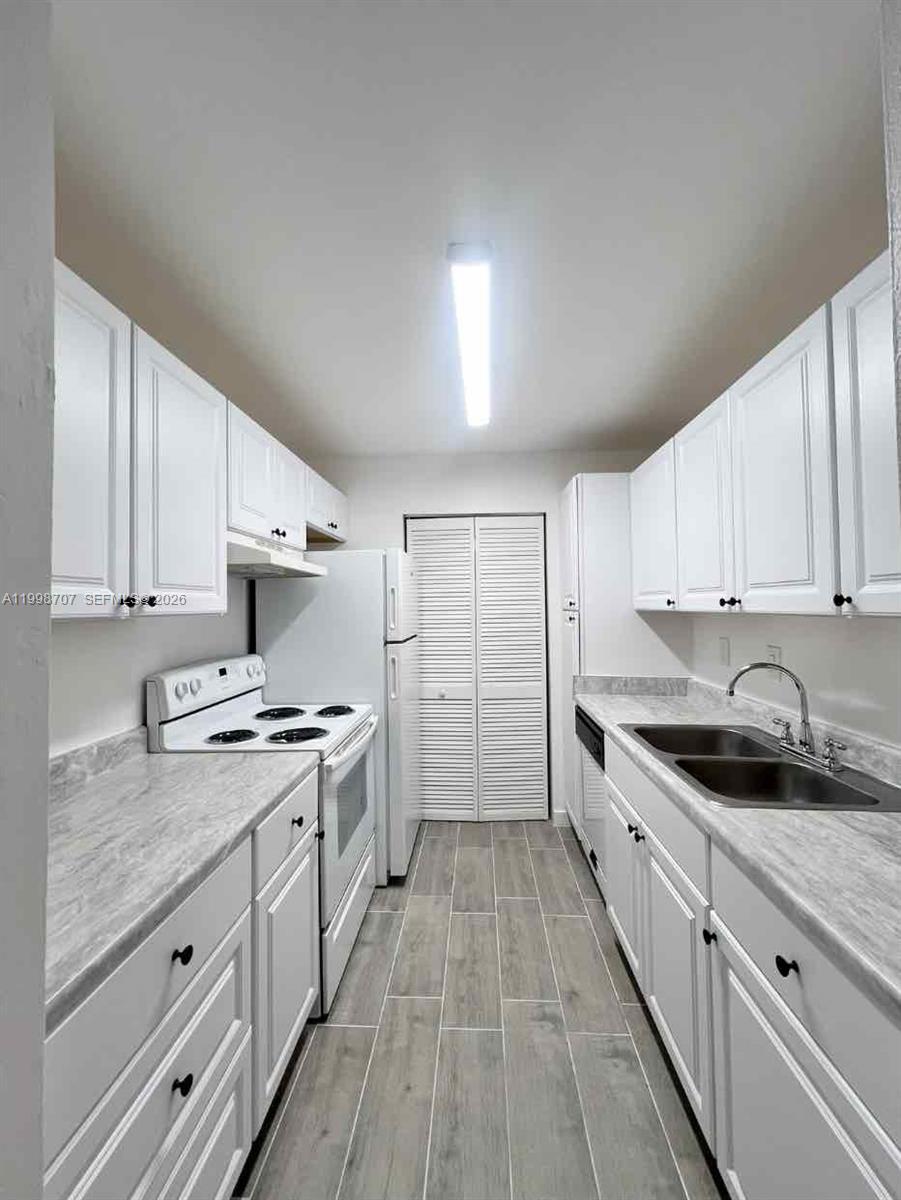 A galley-style kitchen features white cabinets, marble-patterned countertops, and light wood-look tile flooring — 8719 NW 39th St # 8719, Sunrise FL 33351, SUNRISE, FL