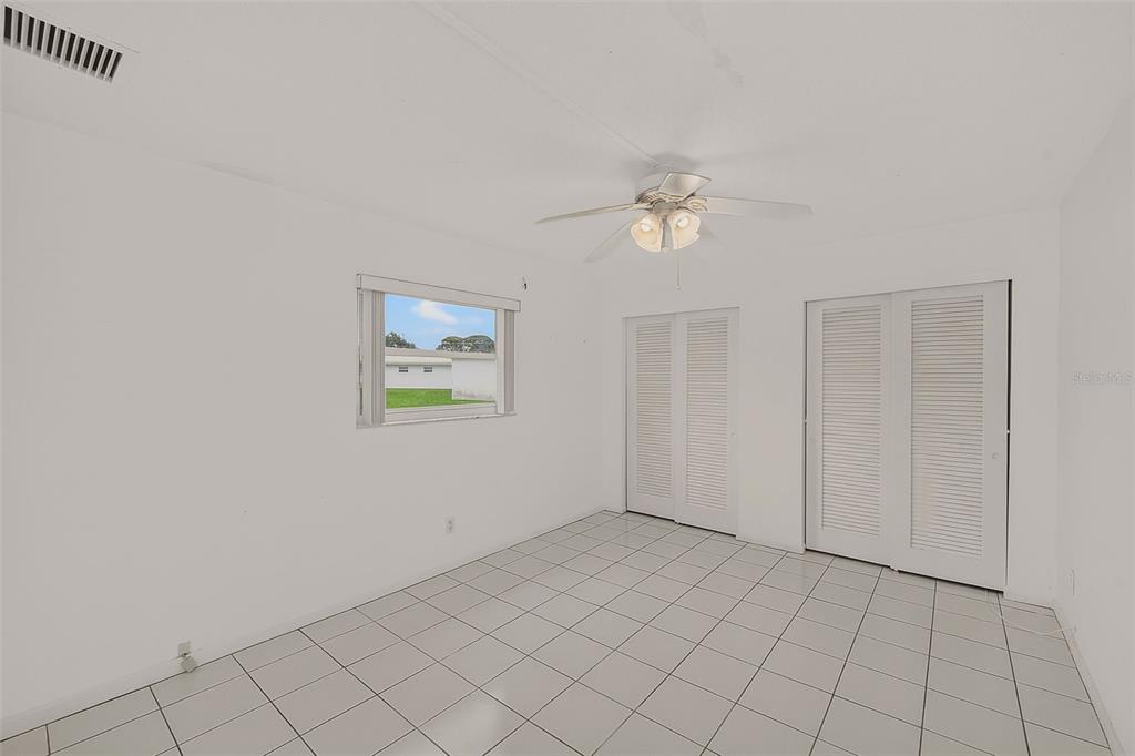 A bedroom with white walls, white tile flooring, a ceiling fan, and two louvered closets — 14144 87TH AVENUE, SEMINOLE, FL