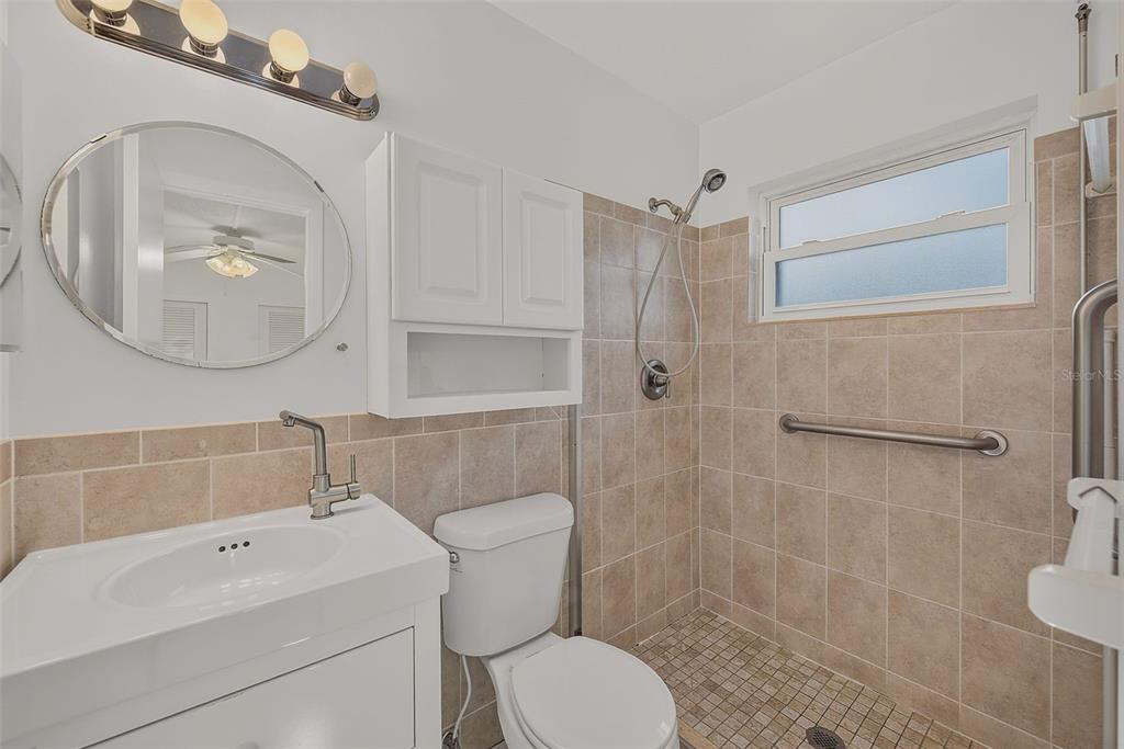 A bathroom featuring a white vanity, a toilet, and a tiled walk-in shower with grab bars — 14144 87TH AVENUE, SEMINOLE, FL