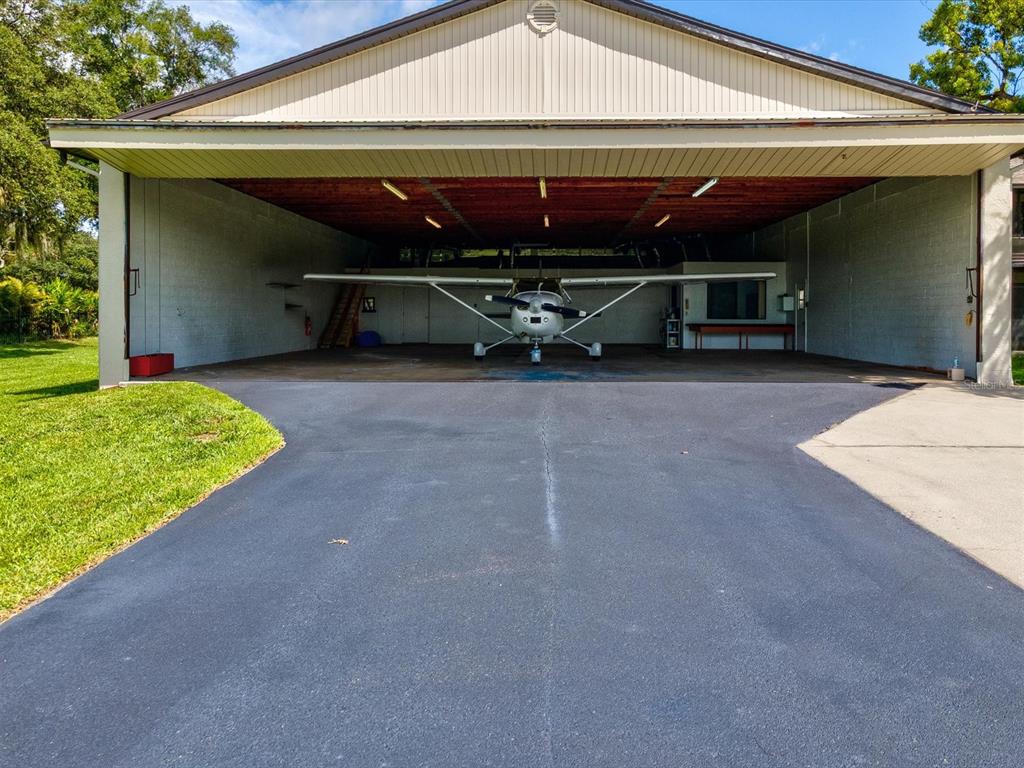 A small airplane is parked inside a large, open-air hangar with a concrete driveway — 8720 AIRWAY BOULEVARD, NEW PORT RICHEY, FL