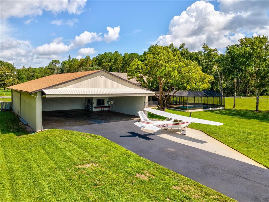 An airplane is parked on a driveway in front of a large hangar and pool — 8720 AIRWAY BOULEVARD, NEW PORT RICHEY, FL