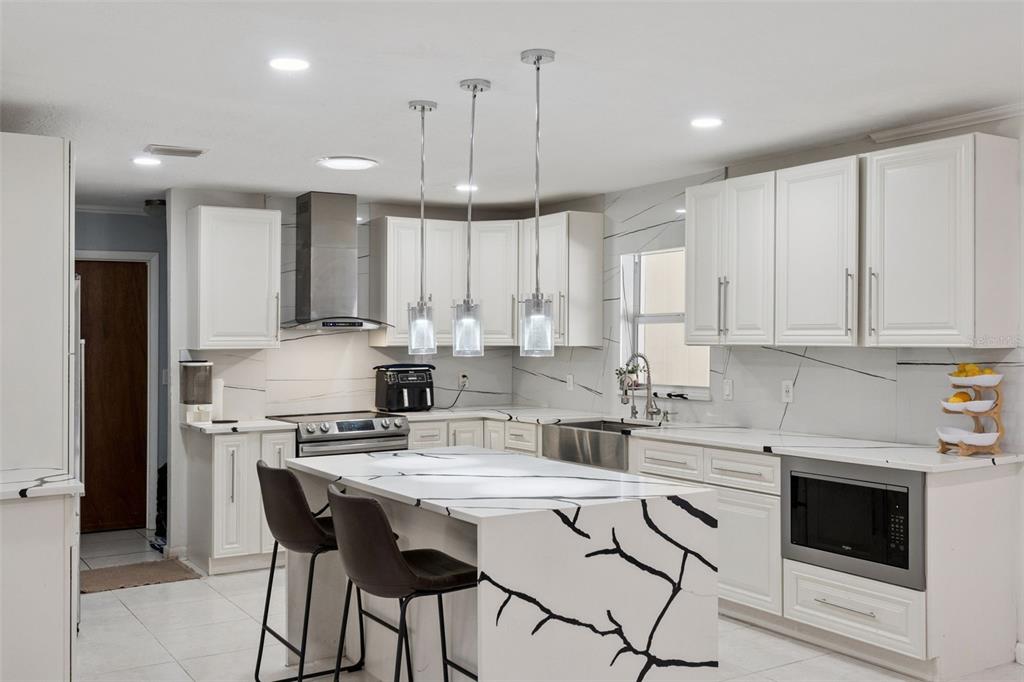 A modern kitchen features white cabinets, a marble-patterned island with seating, and stainless steel appliances — 1756 TANGLE WOOD DRIVE, KISSIMMEE, FL