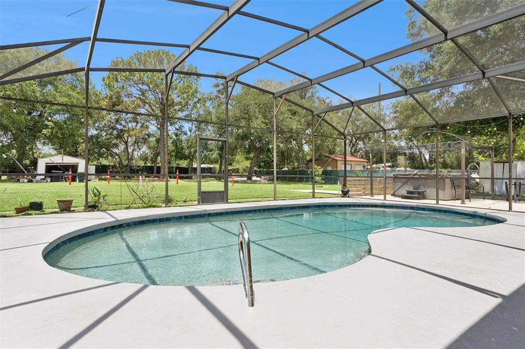 A swimming pool enclosed by a screened lanai overlooks a large, grassy backyard with trees — 1756 TANGLE WOOD DRIVE, KISSIMMEE, FL