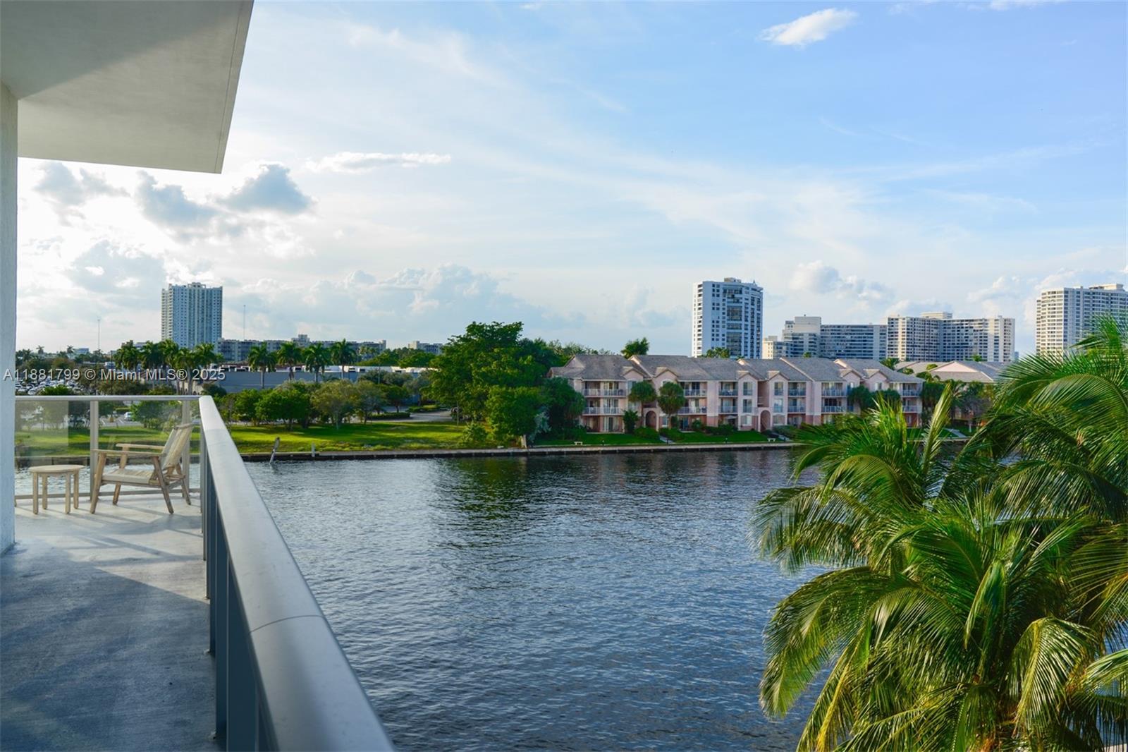 A balcony overlooks a body of water with residential buildings and palm trees in the distance — 4010 S Ocean Dr # R302, Hollywood FL 33019, HOLLYWOOD, FL