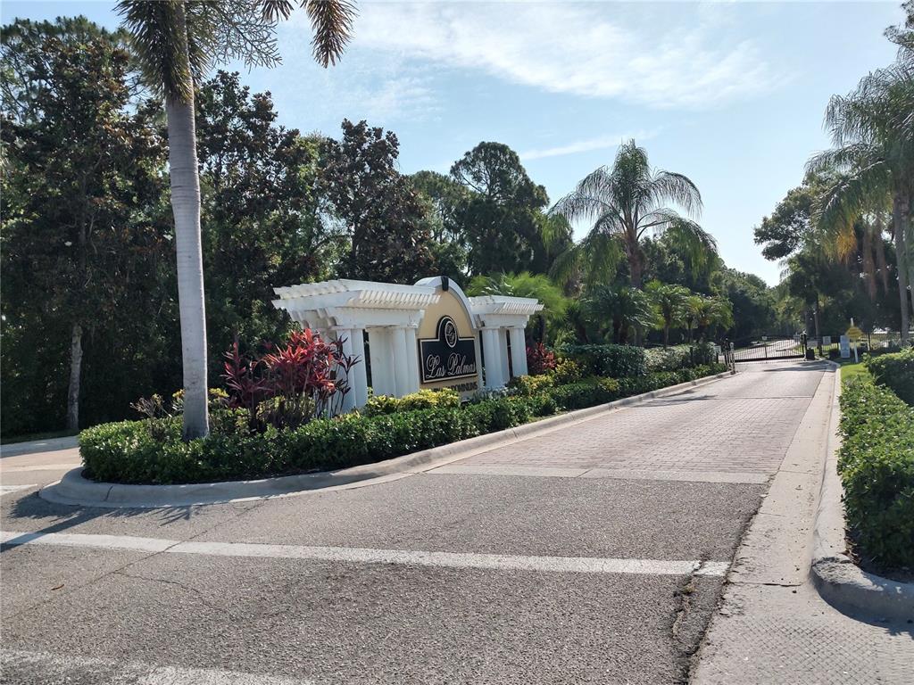 A paved entrance road leads to a Las Palmas community sign with white architectural columns — 5600 BENTGRASS DRIVE UNIT 8-103, SARASOTA, FL