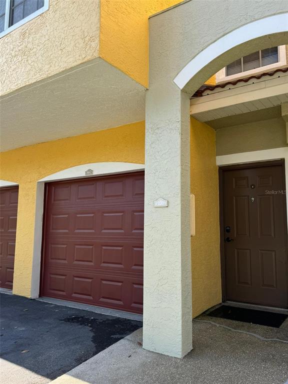 A yellow stucco building exterior features a brown garage door and a brown front door — 5600 BENTGRASS DRIVE UNIT 8-103, SARASOTA, FL