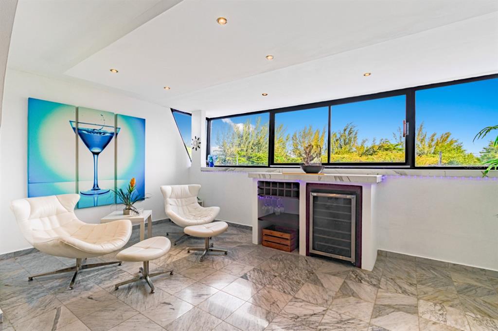 A lounge area with two white chairs, a wine cooler, and large windows overlooking trees — 7185 COND. MAR DE ISLA VERDE UNIT 3A, CAROLINA, PR