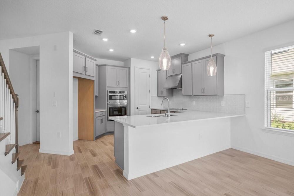 A modern kitchen features gray cabinets, white countertops, a center island, and light wood flooring — 1032 TOP MINNOW ROAD, ST CLOUD, FL