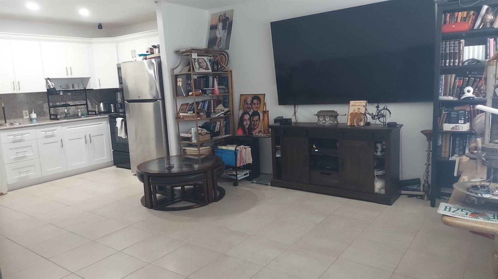 A living room with a large television, media console, and an adjacent open-concept kitchen — 330 Brighton H, Boca Raton FL 33434, BOCA RATON, FL