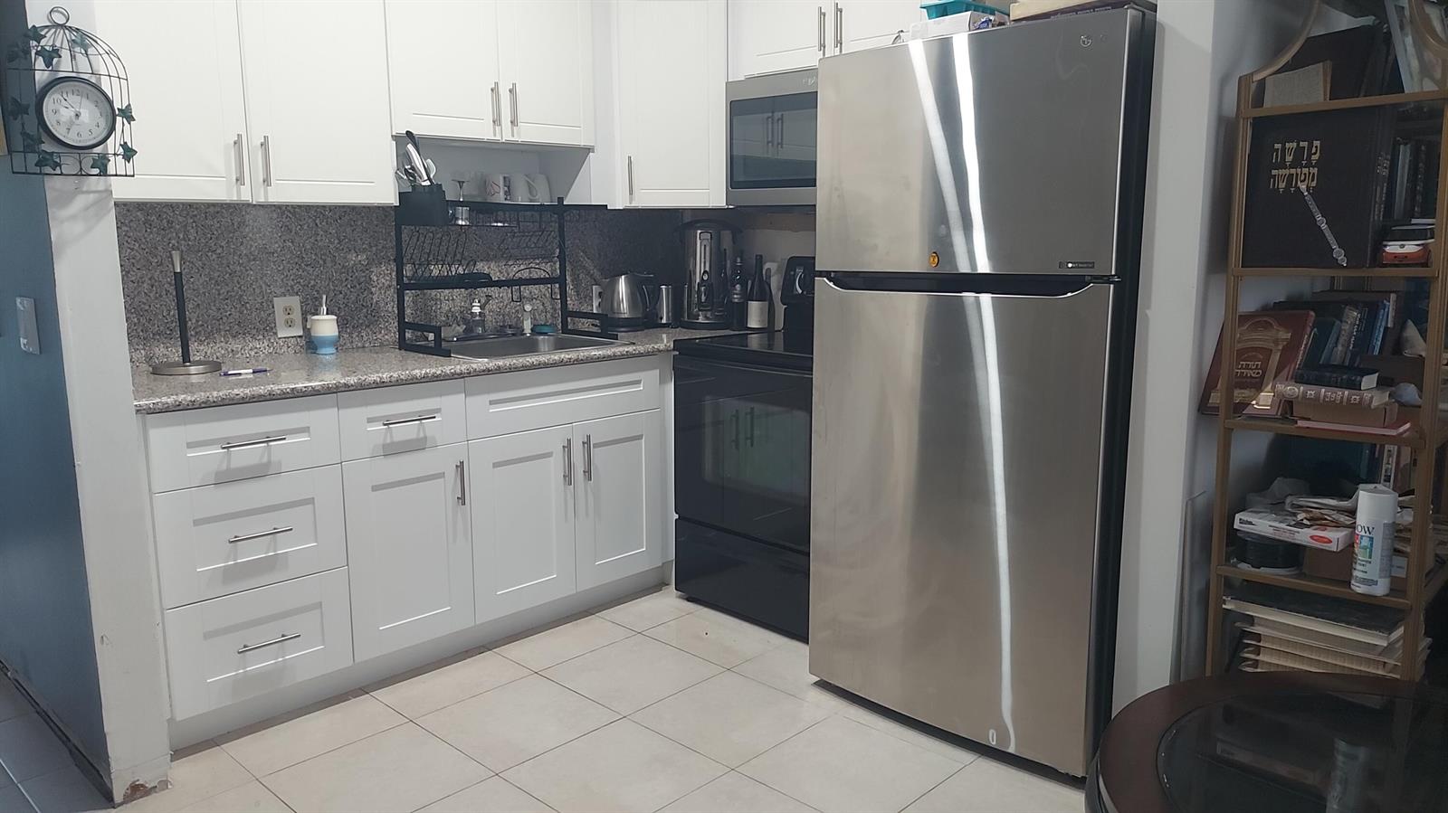 A kitchen features white cabinets, stainless steel appliances, granite countertops, and a tall wooden bookshelf — 330 Brighton H, Boca Raton FL 33434, BOCA RATON, FL