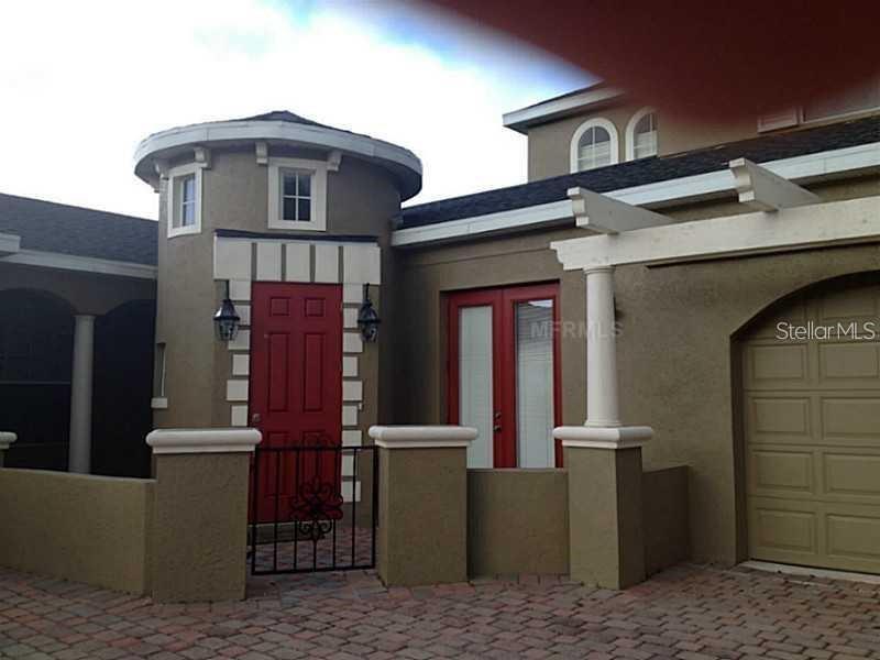 A tan house exterior features a red front door, a turret, and a paved courtyard — 3699 HEIRLOOM ROSE PLACE, OVIEDO, FL