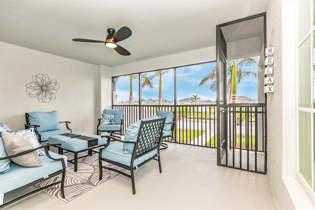 A screened-in patio features light blue cushioned furniture, a ceiling fan, and a metal door — 12550 GALAPAGOS STREET UNIT 204, VENICE, FL