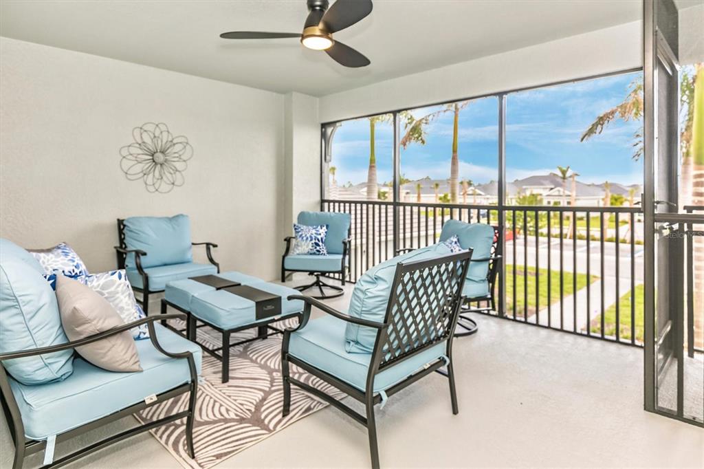 A screened-in balcony features outdoor furniture, a ceiling fan, and views of a neighborhood — 12550 GALAPAGOS STREET UNIT 204, VENICE, FL