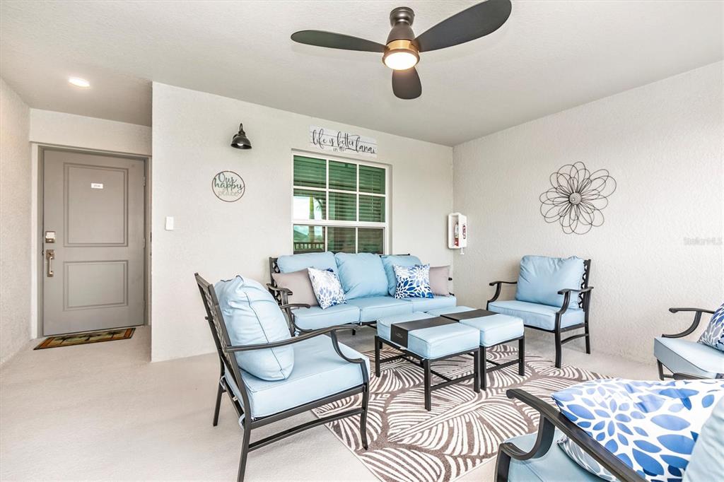 A covered patio features light blue outdoor furniture, a ceiling fan, and a patterned area rug — 12550 GALAPAGOS STREET UNIT 204, VENICE, FL