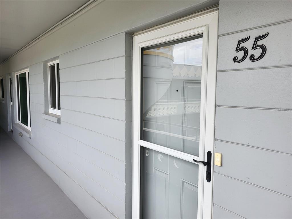 A gray exterior wall features a white storm door labeled with the number 55 — 2341 HAITIAN DRIVE UNIT 55, CLEARWATER, FL