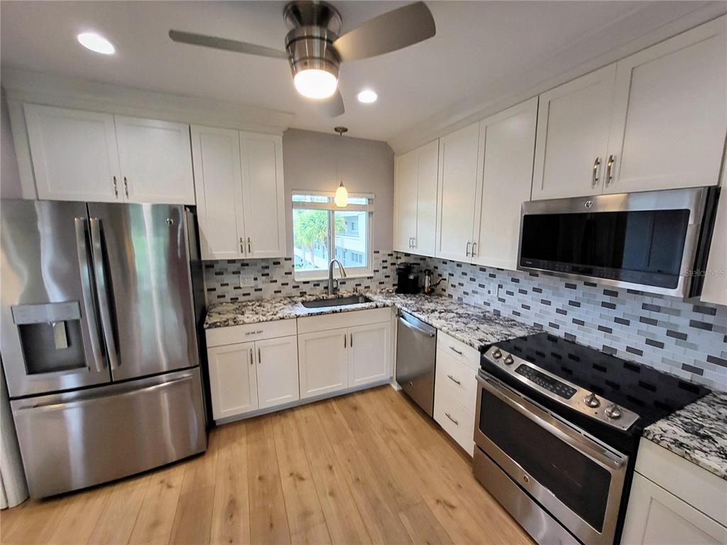 A kitchen features white cabinets, stainless steel appliances, a tiled backsplash, and wood-look flooring — 2341 HAITIAN DRIVE UNIT 55, CLEARWATER, FL