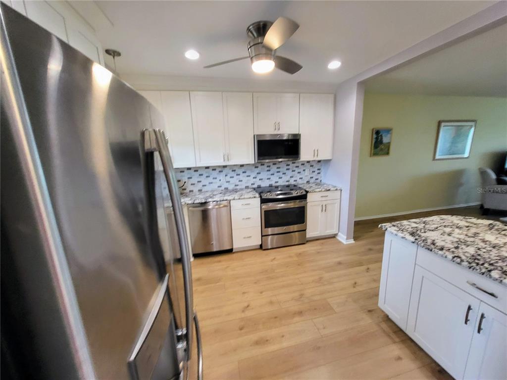 A kitchen features white cabinets, stainless steel appliances, granite countertops, and light wood flooring — 2341 HAITIAN DRIVE UNIT 55, CLEARWATER, FL
