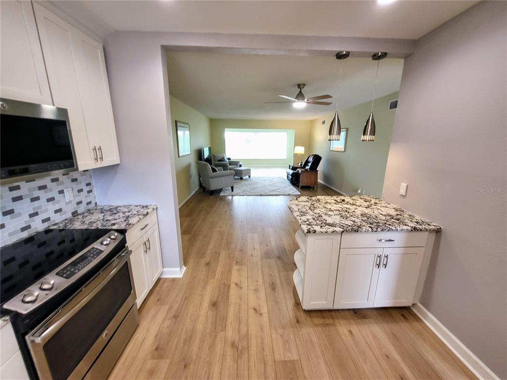 A kitchen with white cabinets and granite countertops opens into a living room area — 2341 HAITIAN DRIVE UNIT 55, CLEARWATER, FL
