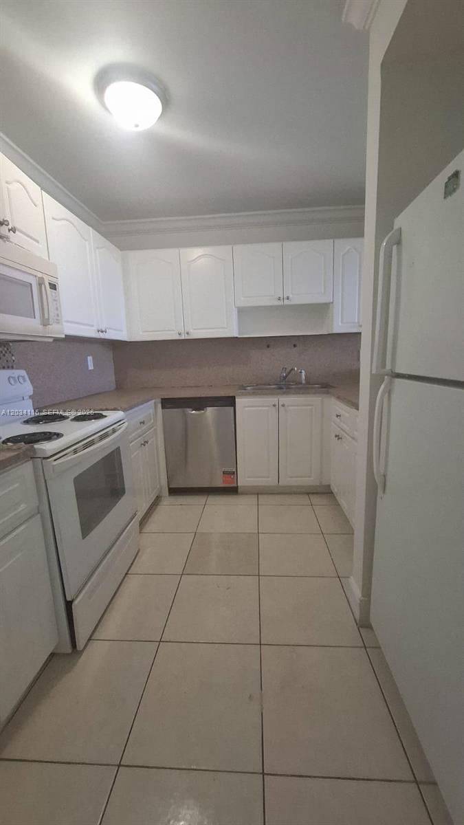 A kitchen features white cabinets, a stainless steel dishwasher, white appliances, and tiled flooring — 6940 Miami Gardens Dr # 522, Hialeah FL 33015, HIALEAH, FL
