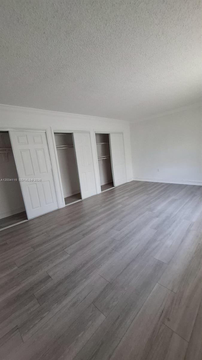 An empty room features light wood-look flooring, white walls, and three sets of closet doors — 6940 Miami Gardens Dr # 522, Hialeah FL 33015, HIALEAH, FL