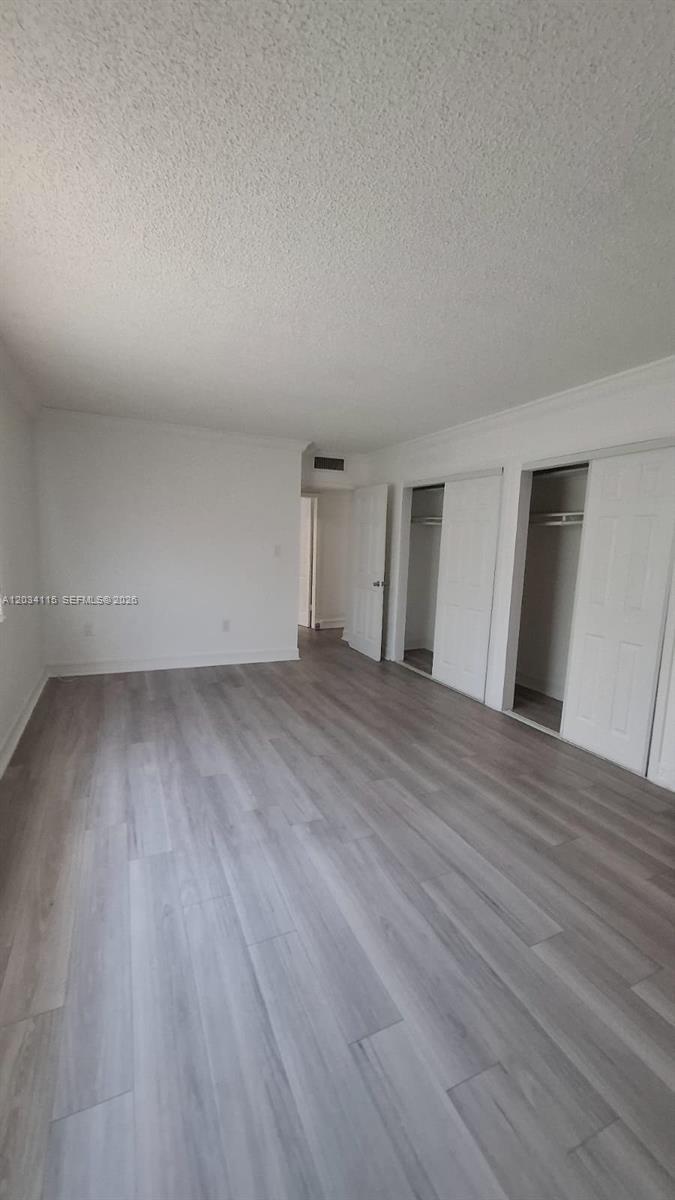 An empty bedroom features light-colored wood-look flooring, white walls, and two sliding closet doors — 6940 Miami Gardens Dr # 522, Hialeah FL 33015, HIALEAH, FL