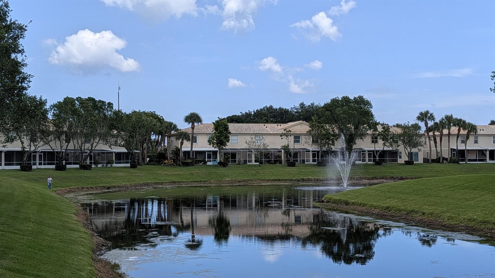 A pond with a fountain sits in front of a row of multi-story residential buildings — 346 Timberwalk Trail, Jupiter FL 33458, JUPITER, FL
