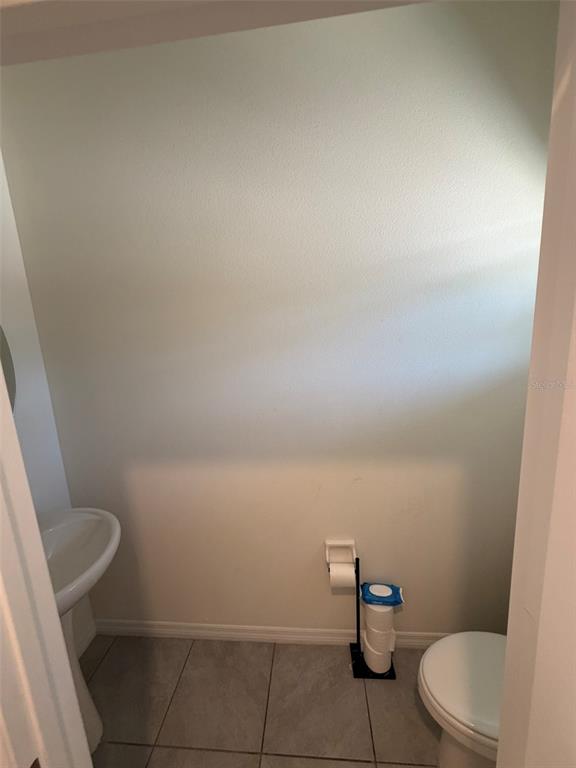 A small powder room features a pedestal sink, a toilet, and light-colored tile flooring — 8860 MILESTONE DRIVE, SARASOTA, FL