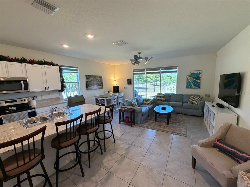 An open-concept kitchen and living area features a granite island, tile floors, and blue sofas — 8860 MILESTONE DRIVE, SARASOTA, FL