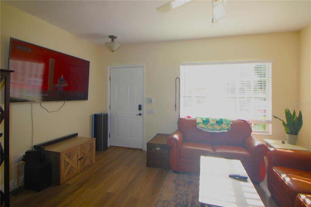 A living room features wood-look flooring, a wall-mounted television, a leather sofa, and a window — 12369 BERKELEY SQUARE DRIVE, TAMPA, FL