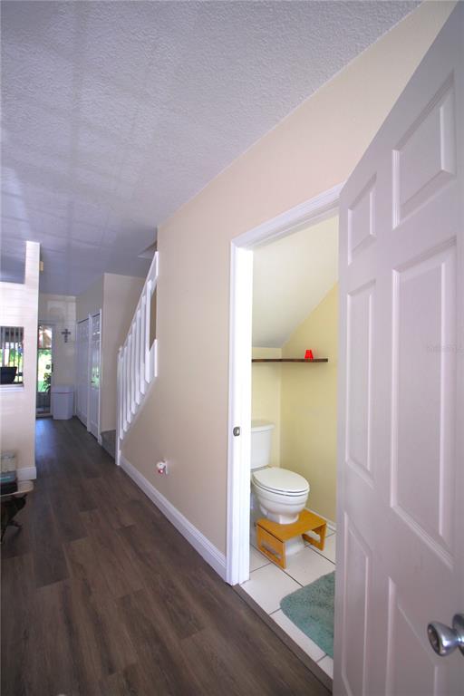 A hallway with wood-look flooring leads to a small bathroom with a toilet and step stool — 12369 BERKELEY SQUARE DRIVE, TAMPA, FL