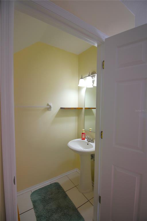 A small bathroom features a pedestal sink, a wall-mounted shelf, and light yellow walls — 12369 BERKELEY SQUARE DRIVE, TAMPA, FL