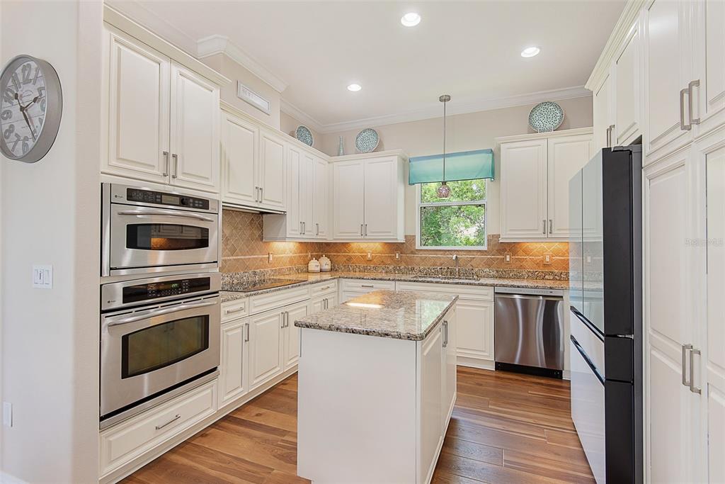 A kitchen features white cabinetry, stainless steel appliances, granite countertops, and wood-look flooring — 27 LONGVIEW WAY N, PALM COAST, FL