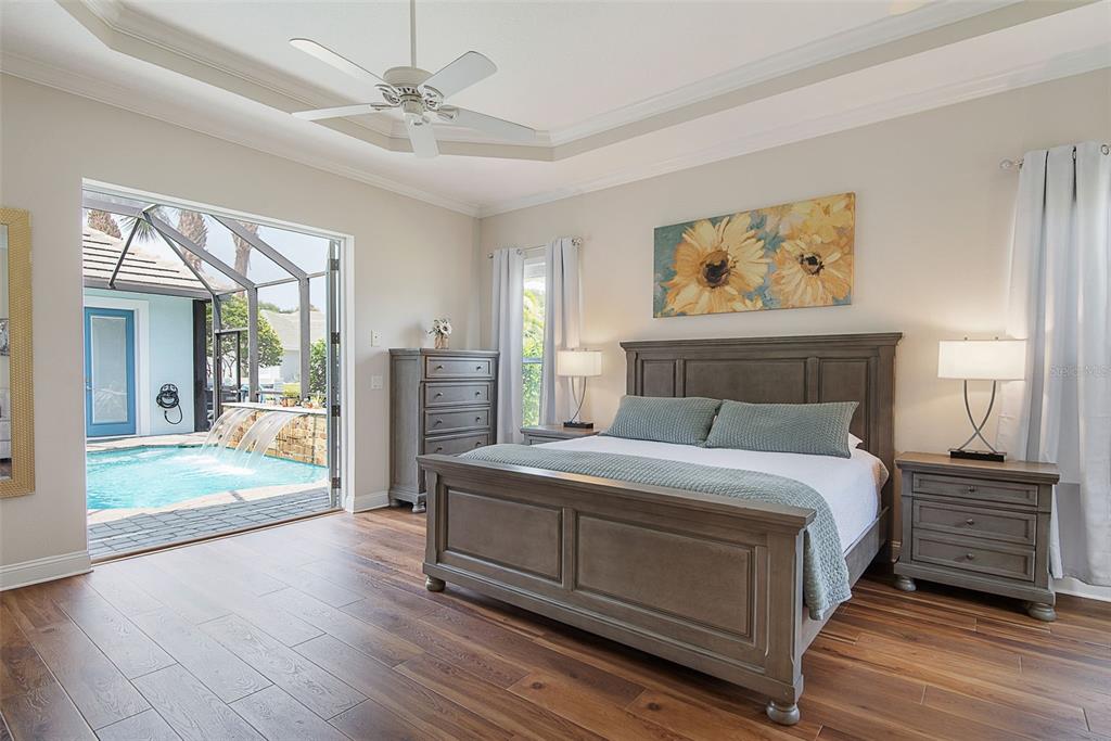 A bedroom with wood floors and a bed faces a sliding door opening to a pool — 27 LONGVIEW WAY N, PALM COAST, FL