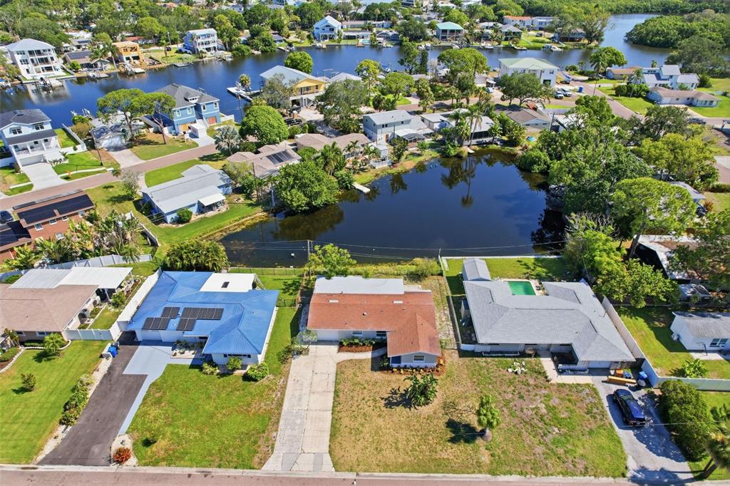 An aerial view shows three houses near a pond and a canal in a neighborhood — 307 87TH AVENUE NE, ST PETERSBURG, FL