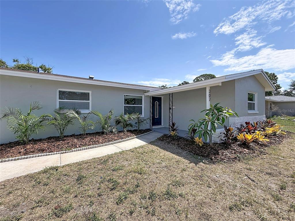 A single-story house with a light-colored exterior, a covered entryway, and landscaped front garden beds — 307 87TH AVENUE NE, ST PETERSBURG, FL