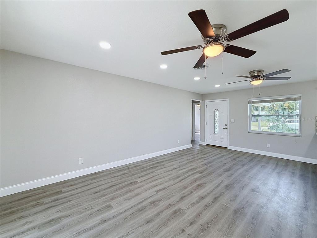A living room with gray walls, wood-look flooring, two ceiling fans, and a front door — 307 87TH AVENUE NE, ST PETERSBURG, FL