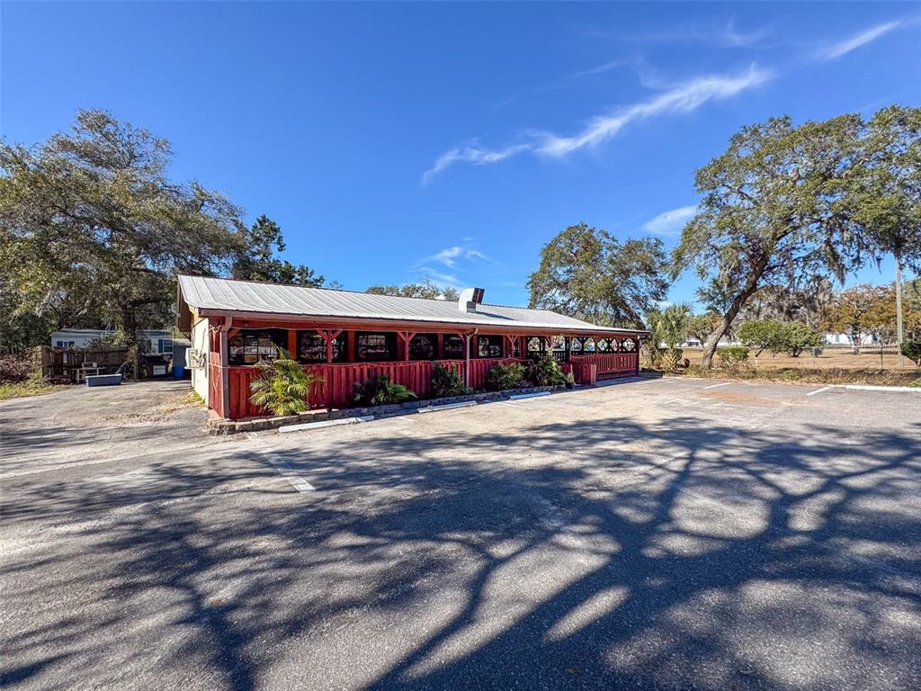 A single-story commercial building with a red exterior and a metal roof sits beside a parking lot — 15525 & 15527 SHADY HILLS ROAD, SHADY HILLS, FL