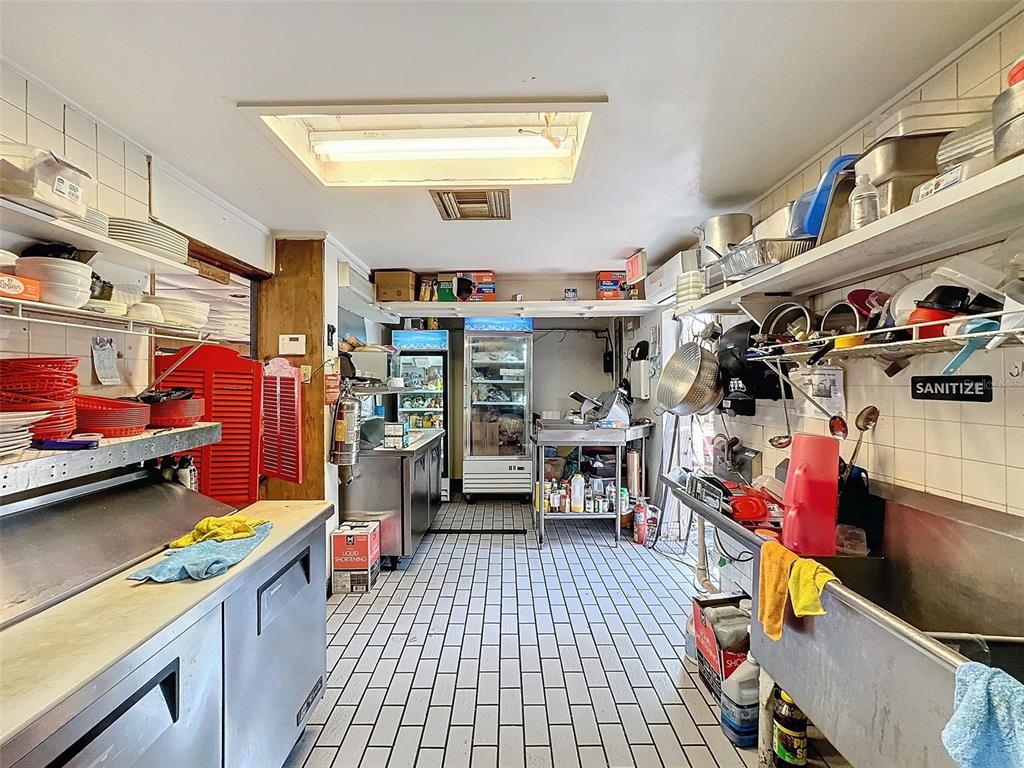 A commercial kitchen features stainless steel equipment, tiled flooring, and open shelving for storage — 15525 & 15527 SHADY HILLS ROAD, SHADY HILLS, FL