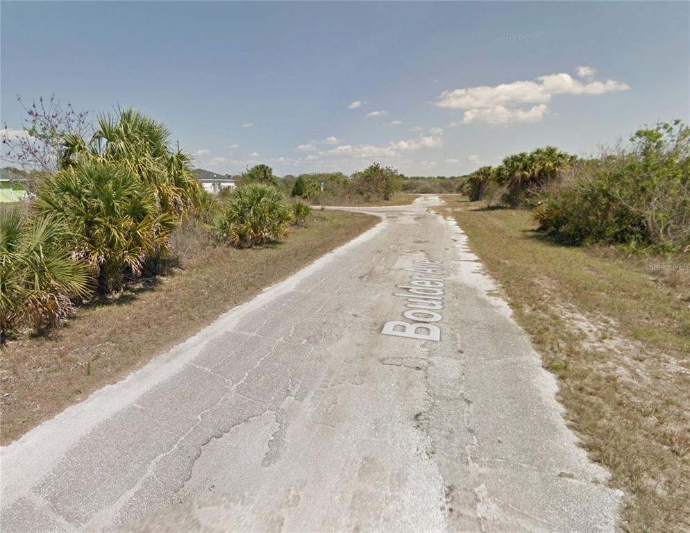 A paved road stretches through a rural, undeveloped area with surrounding palm trees and brush — 19425 BOULDER AVENUE, PORT CHARLOTTE, FL