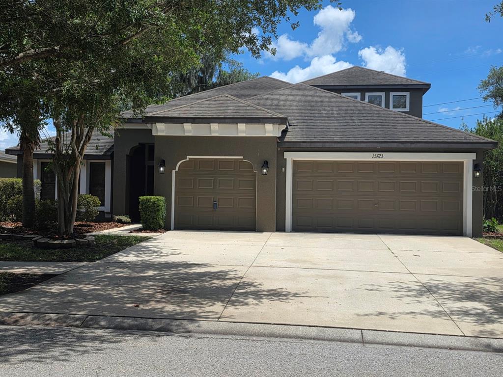 A single-story house with a three-car garage, dark exterior paint, and a concrete driveway — 15723 STARLING WATER DRIVE, LITHIA, FL