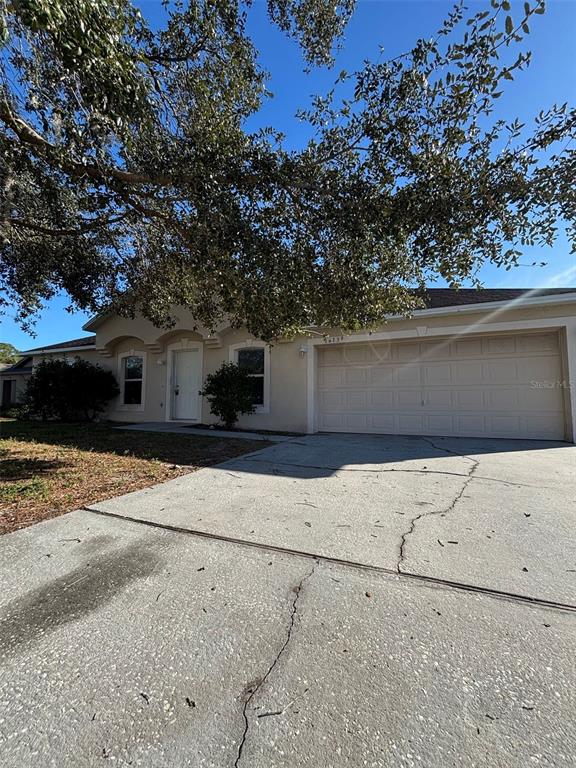 A single-story house with a beige exterior, a two-car garage, and a large shade tree — 1613 SAIL DRIVE, POINCIANA, FL