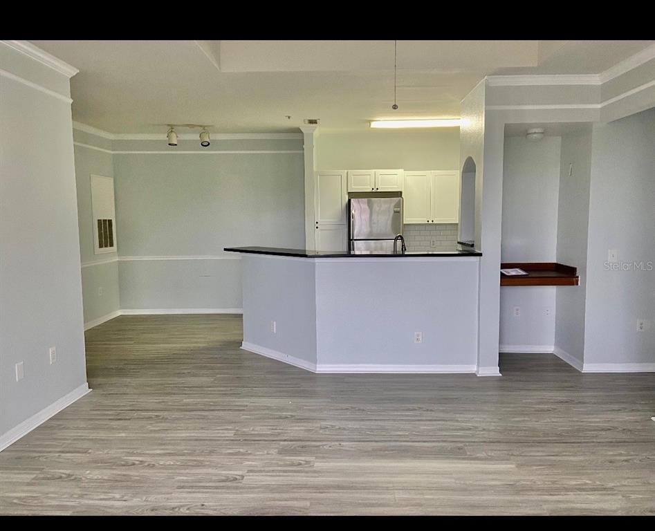 An open-concept kitchen with a breakfast bar, white cabinets, and light wood-look flooring — 6412 QUEENS BOROUGH AVENUE UNIT 315, ORLANDO, FL